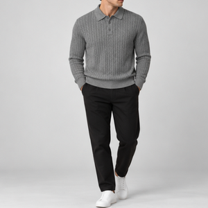 A man wearing a gray cable-knit polo sweater, black trousers, and white sneakers, standing against a light gray studio background.